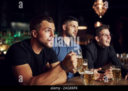 Completamente concentrato. Tre gli appassionati di sport in un bar di guardare partite di calcio. Con la birra in mano Foto Stock