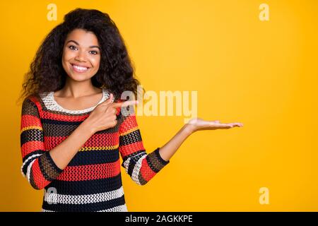 Close-up ritratto di lei bella attraente Allegro vivace-ondulato ragazza dai capelli in maglia maglione dimostrando oggetto invisibile ad isolati su luminose Foto Stock