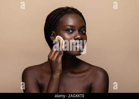 Close up ritratto di un attraente americano africano donna rimuovere il trucco con spugna Foto Stock