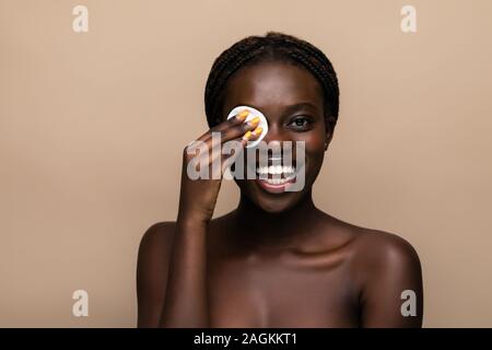 Close up ritratto di un attraente americano africano donna rimuovere il trucco con spugna Foto Stock