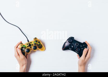 Mani femminili tenendo due gamepad bianco su sfondo di legno piana e composizione di laici. Foto Stock