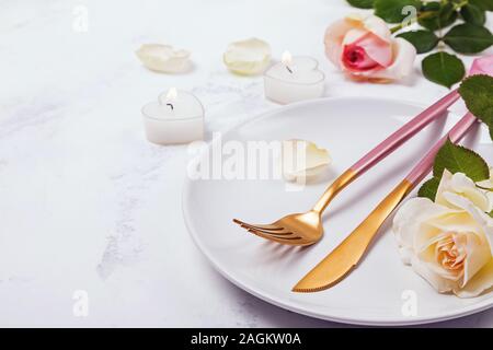Coltello, forchetta e rose nella piastra bianca. Foto Stock