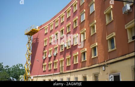 Pittore lavora oltre a Forbice Piattaforma di sollevamento. Urbano su sfondo blu cielo Foto Stock