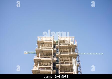 Gru a lavorare sulla parte superiore del nuovo appartamento residenziale edificio. Cielo blu sullo sfondo Foto Stock