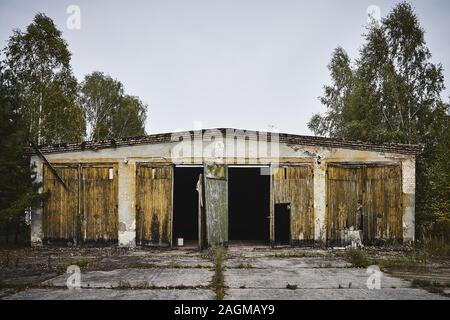 Vecchio magazzino abbandonato con porte rotte circondato da alberi Foto Stock