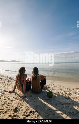 Coppia giovane seduto sulla spiaggia di sabbia e di bere acqua di cocco e guardando il bellissimo mare calmo Foto Stock