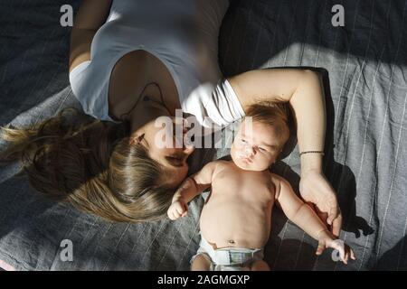 La madre con il figlio neonato sdraiato sul letto in i raggi di luce solare Foto Stock