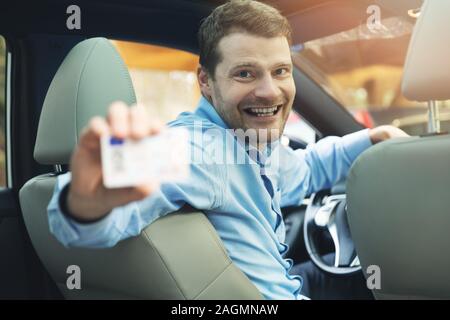 Scuola guida - uomo seduto dentro la macchina e mostrando la sua licenza di pilota Foto Stock