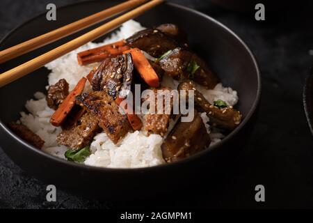 Vegano seitan coreana, le carote e le melanzane friggere riso con kimchi in una ciotola nero Foto Stock