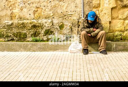 Un povero uomo seduto su un cordolo in pietra con nessun denaro per mangiare e nessun posto dove andare. Foto Stock