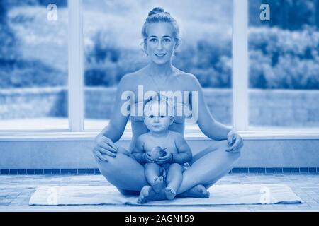 Caucasian il bambino e la madre figlia facendo esercizi di fitness seduta di yoga in lotus pongono guardando la fotocamera. Il Toddler eating apple. Famiglia Sport insieme. Foto Stock