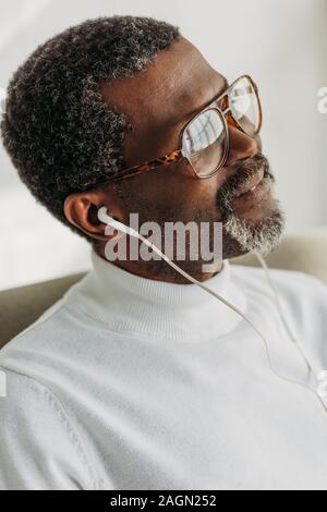 Trasognata African American uomo in bicchieri ascoltando musica in cuffia Foto Stock