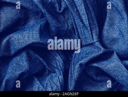 Closeup blu classico macro texture di jeans blu materiale di tessuto o indumenti. Tonica trendy anno 2020 colore di sfondo con le rughe e le pieghe. Dark bl Foto Stock