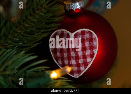 Un rosso scubolo con un cuore rosso di gingham appeso in un albero di Natale artificiale Foto Stock