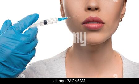 Le mani di un medico di guanti in lattice blu dando il labbro di iniezione con una siringa a donna isolato su sfondo bianco Foto Stock