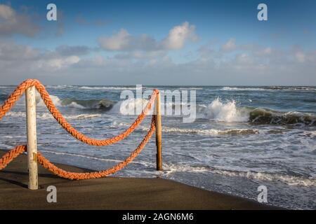Nel tardo pomeriggio sulla spiaggia, sul mare il bordo con il recinto di corda che guarda al mare con onde che si infrangono Foto Stock