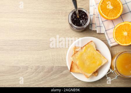 Toast sulla piastra, marmellata, asciugamano e arancione su sfondo di legno, vista dall'alto Foto Stock