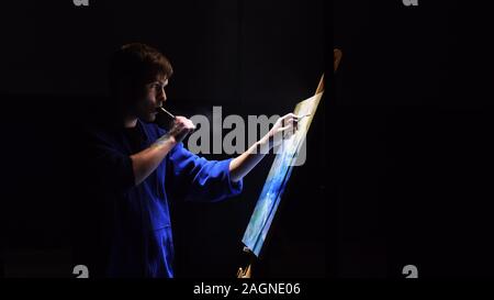 Artista copista paint seascape con nave in oceano. Fumo Vaper vape e-sigaretta. Artigiano arredatore disegnare come barca vela sul mare blu con colori acrilici. Foto Stock
