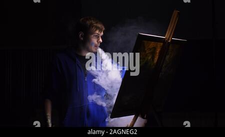 Artista copista paint seascape con nave in oceano. Fumo Vaper vape e-sigaretta. Artigiano arredatore disegnare come barca vela sul mare blu con colori acrilici. Foto Stock
