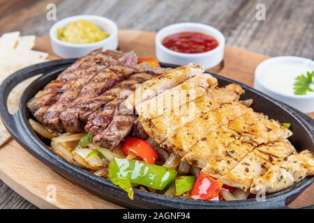 Per Fajita Combo; bistecca messicana e fajitas di pollo nella padella di ferro con peperoni e cipolla shot con una calda luce colorata Foto Stock