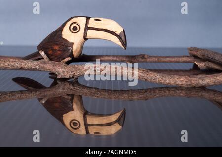 Bella di legno fatti a mano tucan ornamento su e la superficie riflettente su un bachground colorati. Foto Stock