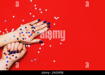 Donna mani con manicure blu su sfondo rosso con stelle multicolore spruzza. Holiday, party e concetto di Natale. Foto Stock