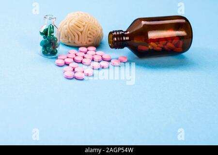 Cervello su uno sfondo blu con rosa e verde pillole in una bottiglia di vetro. Alcune pillole per il cervello. Simbolico per i medicinali, psychopharmaceuticals Foto Stock