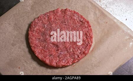 Cuocere rende Medaglioni di carne per gli hamburger. Chef in nero guanti di cibo rende cotoletta. Cotolette siano livellati in acciaio anello in ancora un medaglione. Foto Stock