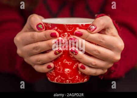 Donna di mano che tiene un rosso tazza di caffè. Con una bella manicure d'inverno. Foto Stock