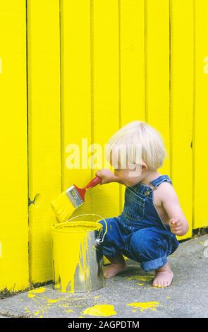 Due anni di vecchio ragazzo di verniciatura di un recinto giallo Foto Stock