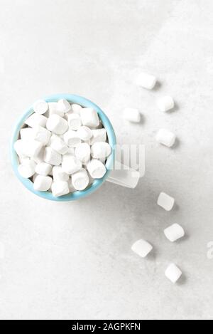 Un boccale di bianco con bordo blu riempita con mini marshmallows bianco su un grigio chiaro la superficie della piastrella. Foto Stock