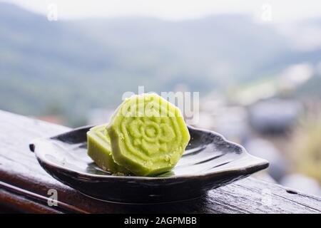 Deliziosa green Mung bean torta con tè nero piastra sulla ringhiera in legno di una piccola locanda di Taiwan con il bel paesaggio di sfondo, vicino. Foto Stock