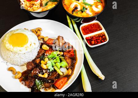 In stile thailandese Kung Bao pollo, servita con jasmine riso bianco, sunny-lato uovo e due ciotole di Tom Yum zuppa. Thailandia piatti tradizionali alimenti sulla scheda Foto Stock