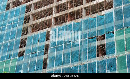 Alto edificio in costruzione, con struttura in metallo e rack di rete di sicurezza che copre l'esterno. Foto Stock