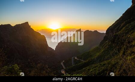 Spagna, Tenerife, arancione tramonto Cielo sopra vista magica oltre masca canyon e strada di montagna tra piante verdi montagne coperte Foto Stock