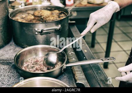 Lo chef è la frittura fette di agnello in olio, cucina commerciale, tonica immagine Foto Stock