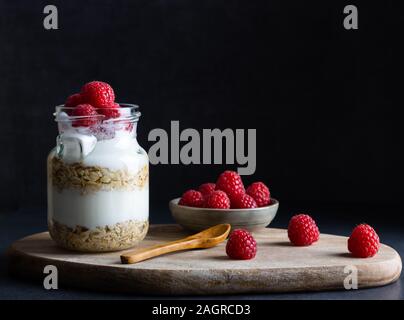 Una sana colazione vegana di yogurt con muesli e lampone su uno sfondo scuro con spazio di copia Foto Stock