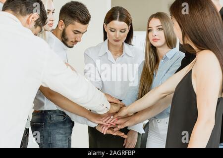 Compagnia dei giovani lavoratori a basso angolo di vista Mani di impilamento insieme in ufficio Foto Stock
