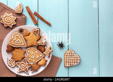 Biscotti allo zenzero decorate con la ciliegina su una piastra su un blu sullo sfondo di legno. Vista superiore, posto per il testo. Foto Stock