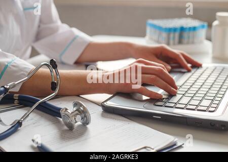 Femmina diagnostician medico al suo posto di lavoro in ospedale. Funziona su computer portatile con raggi x e test medici. Foto Stock