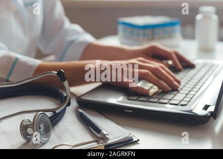 Femmina diagnostician medico al suo posto di lavoro in ospedale. Funziona su computer portatile con raggi x e test medici. Foto Stock