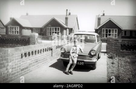 Fotografia o stampa fotografica in bianco e nero di un ragazzo, Terry Waller, di circa 8 anni, appoggiato sul cofano della nuova Ford Anglia di sua madre nel 1960, a St Annes on Sea, Lancashire, Inghilterra, Regno Unito. Foto scattata con una fotocamera Brownie 127, quindi la qualità è limitata. Foto Stock