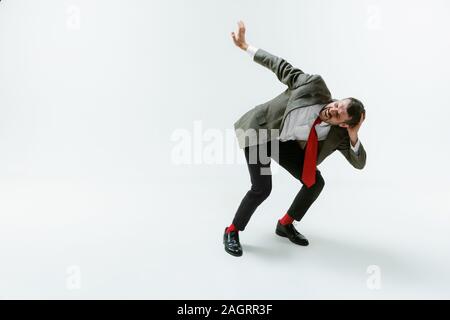 Giovane uomo caucasico flessibili mobili bianco su sfondo per studio. Modello maschile in ufficio wear piegarsi evitando qualcosa, catturato in movimento e di azione. Guarda arrabbiato, spaventata, combattimenti. Emozioni. Foto Stock