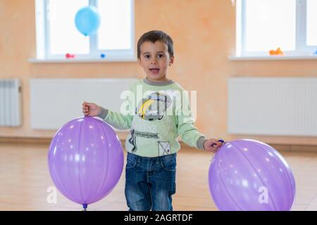 Ragazzino con grande palloncini. Capretto felice con palloncini viola nella hall. Foto Stock