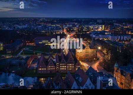 Antenna vista notturna della città illuminata di Lubecca, Germania in inverno con Holstentor e storiche case Salzspeicher, esposizione di lungo periodo a blue h Foto Stock