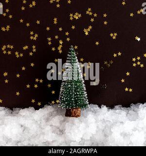 Miniatura di Natale sulla neve e lo sfondo scuro con stelle luccicanti con copia spazio. Composizione di natale, modello di cartolina Foto Stock