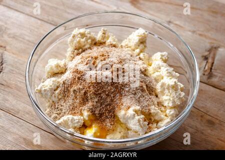 La miscela grezza per la produzione di ricotta torte in recipiente di vetro sul vecchio naturale sfondo di legno vicino la vista. Selective soft focus. Concetto di colazione Foto Stock