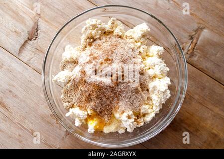 La miscela grezza per la produzione di ricotta torte in recipiente di vetro sul vecchio naturale sfondo di legno vicino la vista. Selective soft focus. Concetto di colazione Foto Stock