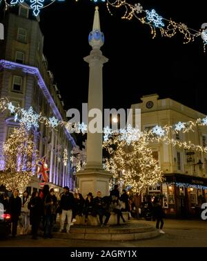 Persone sedersi sulla meridiana monumento di Seven Dials con le luci di Natale infilate sopra e dietro. Il Covent Garden di Londra. Foto Stock