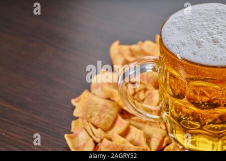 Birra leggera o birra light in un bicchiere e chip su sfondo di legno Foto Stock